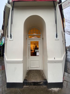 White door with glass panel and white frame. Pull from metal handle on left to open. Doorbell right of door.