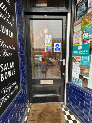 From street, facing venue. Glass door with black, wooden frame ahead. Push silver handle on right to open.
