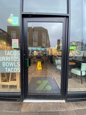Facing glass door with black frame. Push handle on left to open.