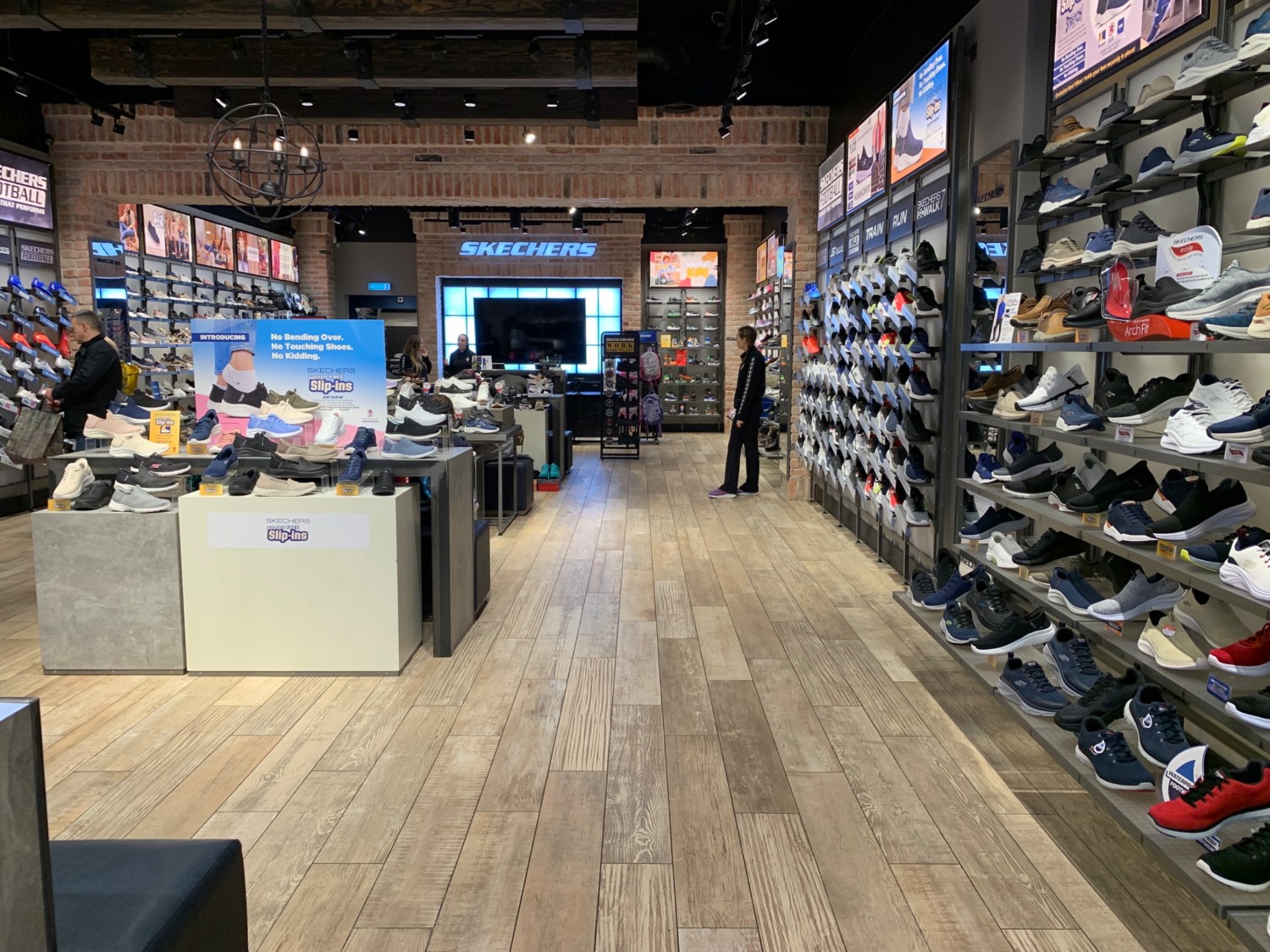 From product shelves facing left. Display tables and stools along left. Path in middle to counter. Product shelves along right.