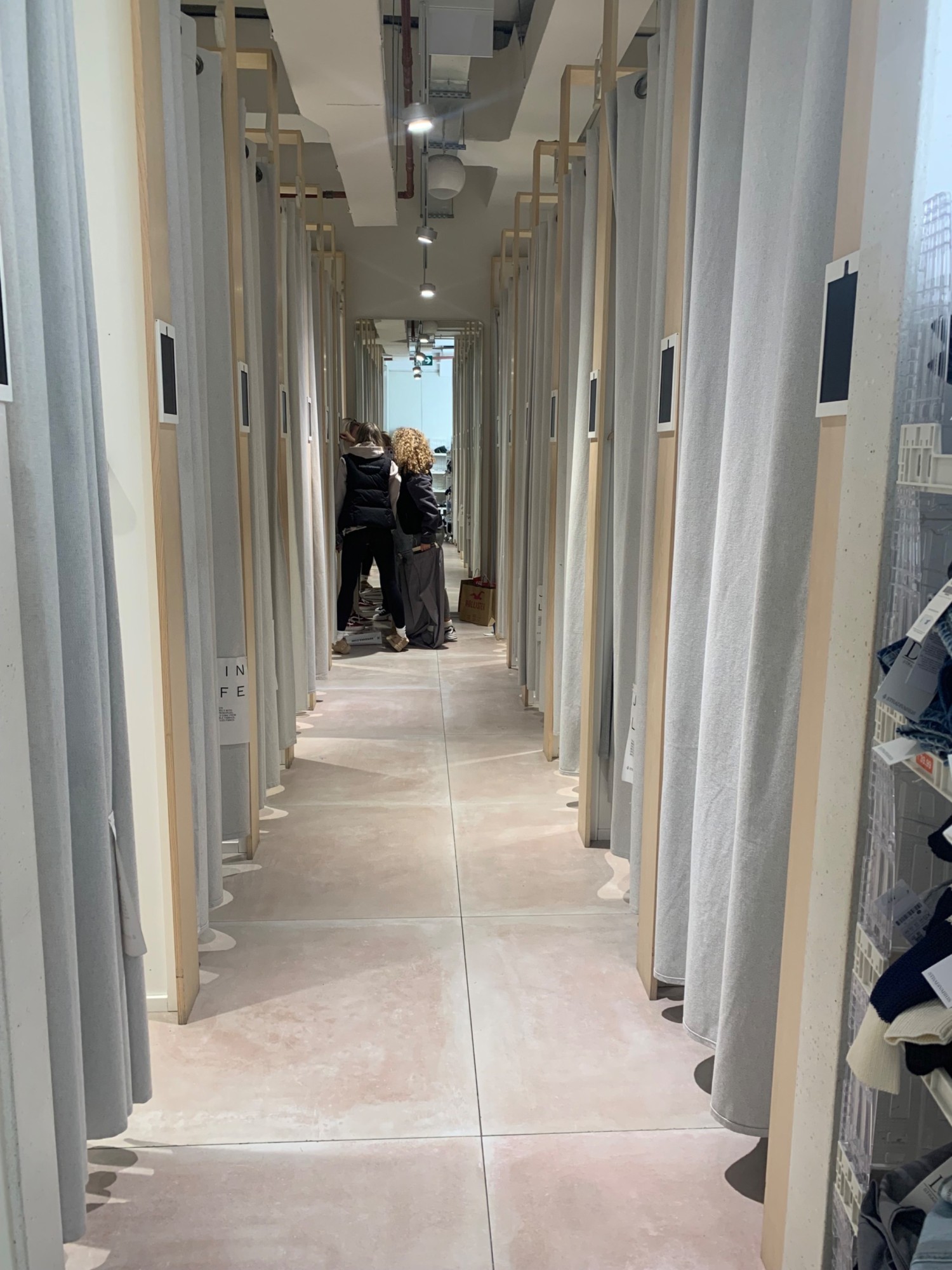 From after counter, facing right. Fitting cubicles along both sides. Accessible fitting room first on left.