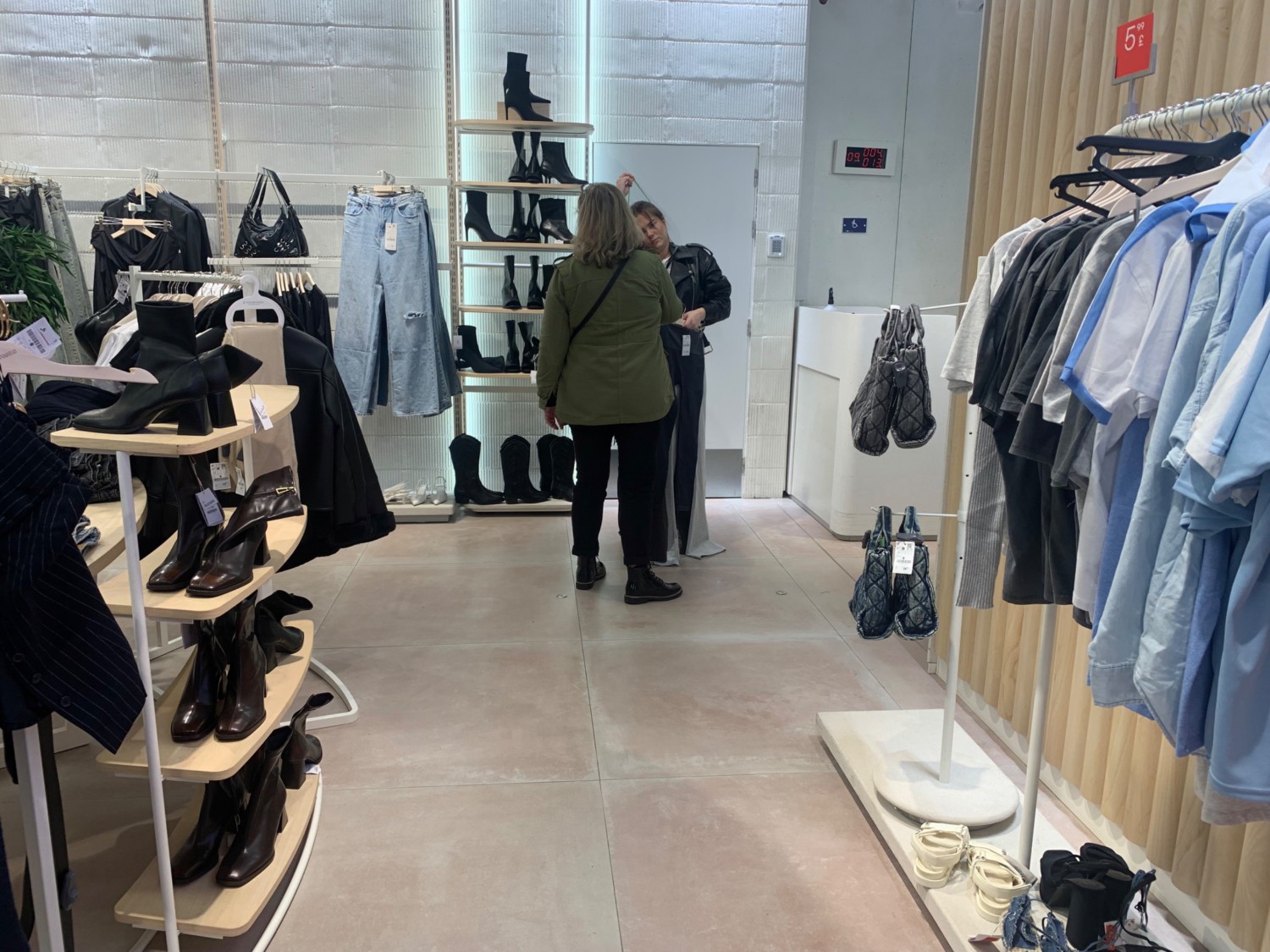 From end of path facing left. Clothing racks along left and right. Path in centre to fitting room archway on back right.