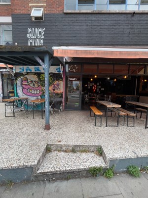 From sidewalk facing venue. Path down center to entrance on back. Pillar on left. Outdoors seating on both sides.