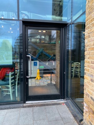 Single glass door in black metal frame. Push silver metal vertical handle from left to open.