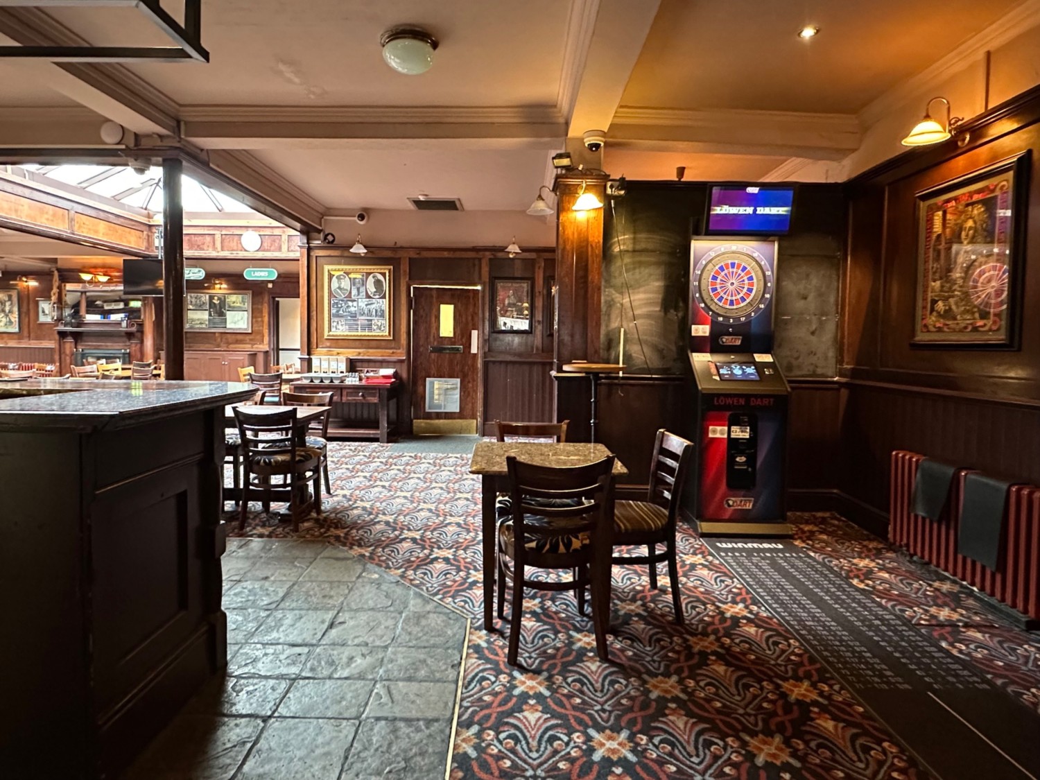 From the second column facing straight. Tables and chairs ahead. Staff counter at left. Dart stand to back right.