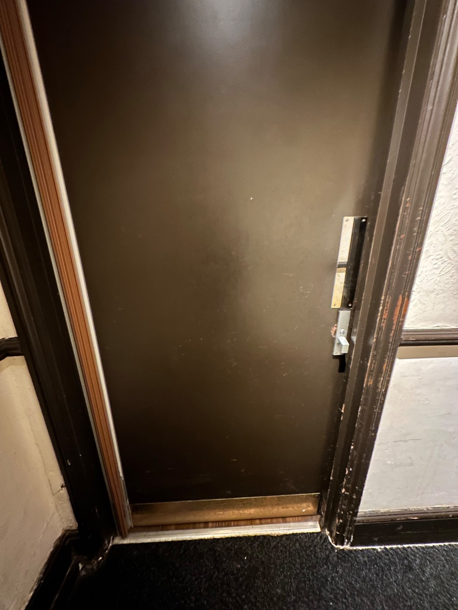 From end of path facing right. Brown bathroom door ahead. Push silver handle from right to open.