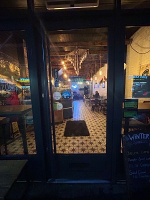 Facing glass door with gray frame. Push on left to open.