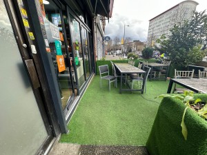 From street, facing venue. Opening ahead to grass floored outdoor seating. Doorway on left.