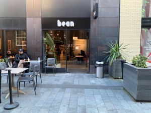 From street, facing venue. Planters along right. Doorway at back. Outdoor seating on left.