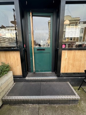Green door ahead with glass panel and black doorframe. Pull long wooden handle on left to open.