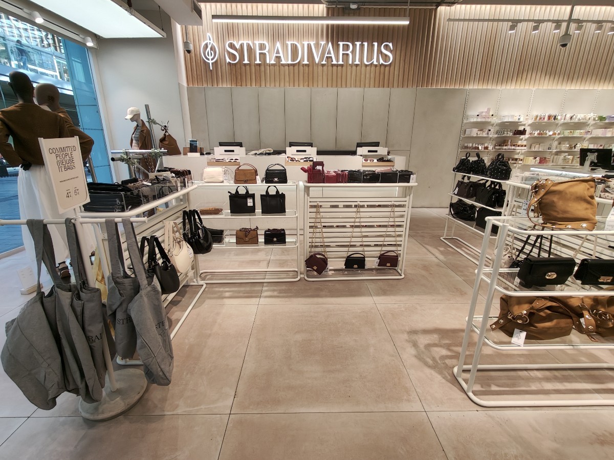 From end of clothing racks facing straight. Path ahead weaving between product shelves to service counter at back.
