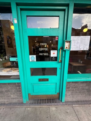 Green door with glass panels and gold handle. Push from right to open.