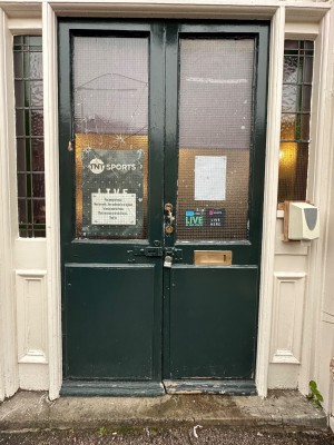 Green and glass panelled double doors. Latch handle to centre of right-hand door. Push to open.