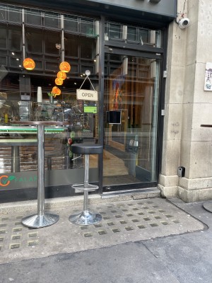 Photo of shopfront with a few tables and stool. Step to entrance. Push door.