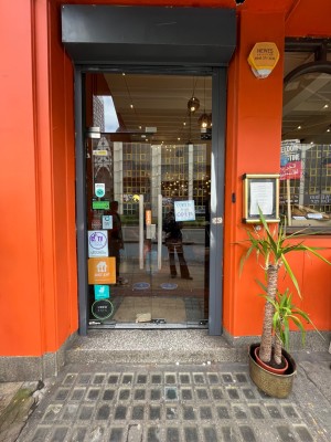 Facing main entrance. Double glass doors with black metal frame, set in orange wall. Long silver  handles. Pull from centre to open.
