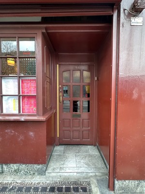 Archway ahead followed by short path to the first set of door. Wooden glass paneled door with handle at left. Push to open.