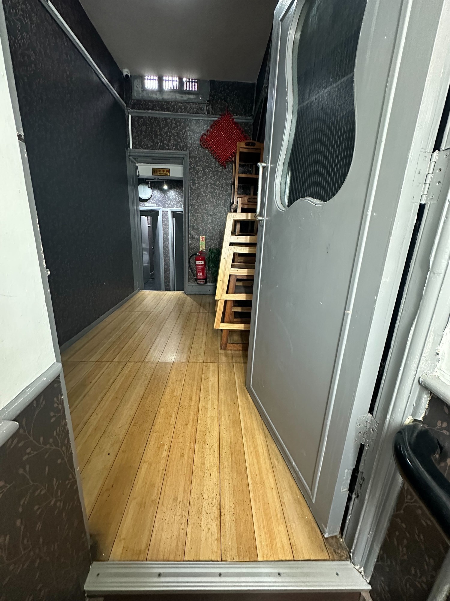 From top of staircase facing straight. Grey door ahead. Push via high metal handle on left to open.