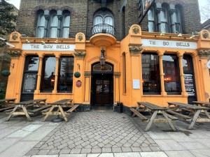 Orange walls with a wooden door. Outdoor seating on left and right of the entrance.