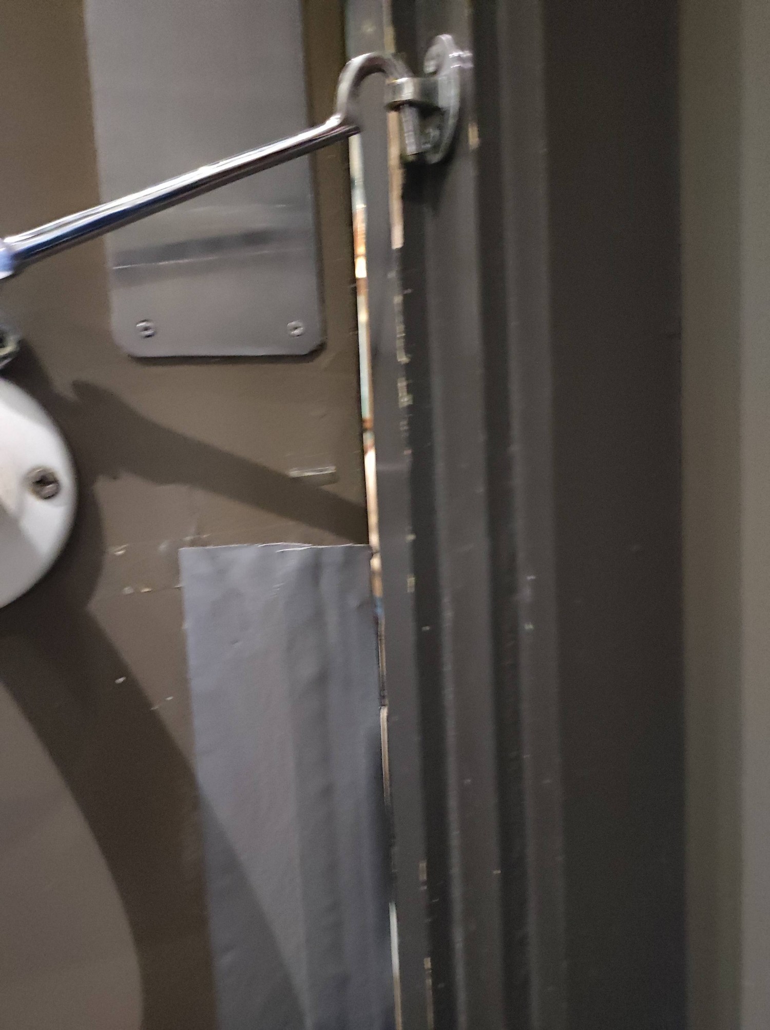 Door secured with a hook and eye latch with a chink between the door and the frame. Tables from main area can be seen through the chink.