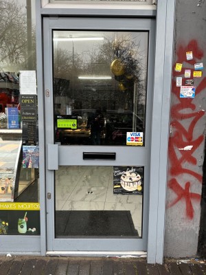 Glass door with grey frame. Push from grey handle on left to open.
