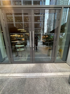 Glass doors with grey, metal frames ahead. Pull silver handles in middle to open.