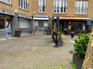 From sidewalk facing straight to venue. Pathway straight ahead. Plant pots along right of path.