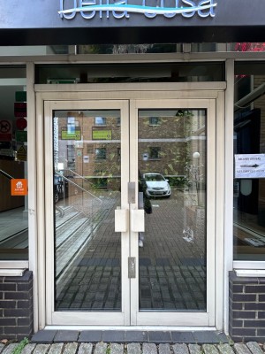 Glass doors with white metal frame ahead. Pull handles in middle to open.