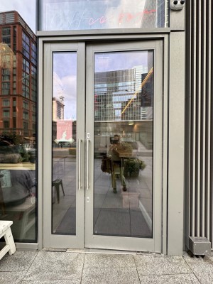 Glass doors with grey, metal frame ahead. Push silver handles in middle to open.