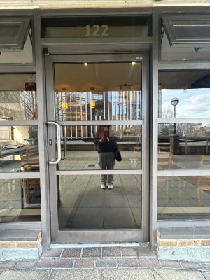 Single glass door with grey frame. Push handle on left to open.