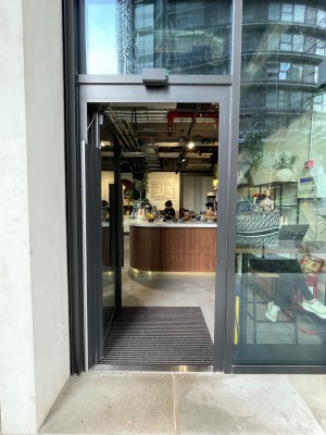 Glass door with grey frame ahead. Push vertical handle on right to open.
