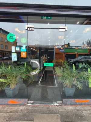 Facing entrance to main area. Single glass door. Plants on both sides of door. Push silver handle on left to open.