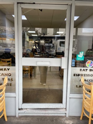 From sidewalk facing entrance. Grey metal framed glass door ahead. Push handle on right to open inwards.