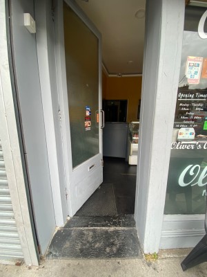 From street facing entrance. White wooden framed glass door ahead. Push handle on right to open inwards.