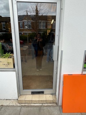 Glass door with grey metal frame. Push vertical handle on right to open.