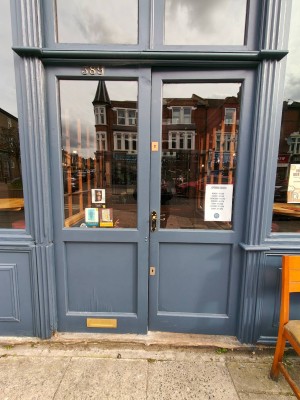 Grey framed double doors. Push golden handle on left of right door to enter.