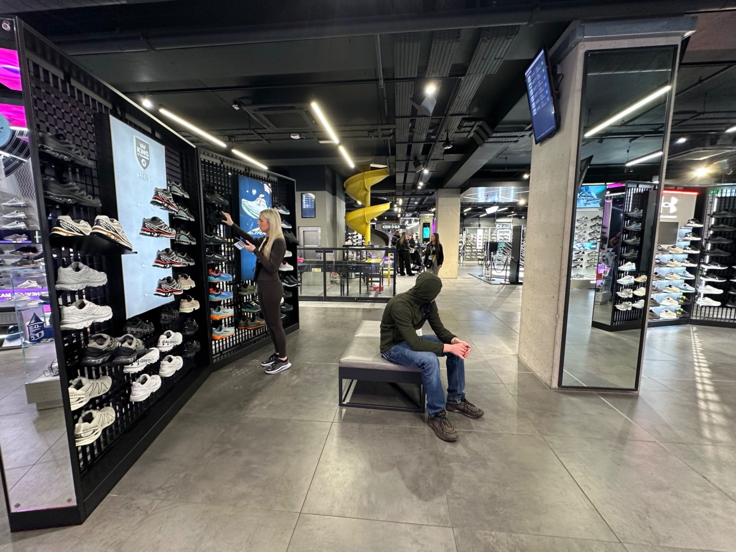 From glass boxes facing right. Mirrored pillar to far right. Bench ahead. Second central Shoe rack along left. Shoe slide to far left corner.
