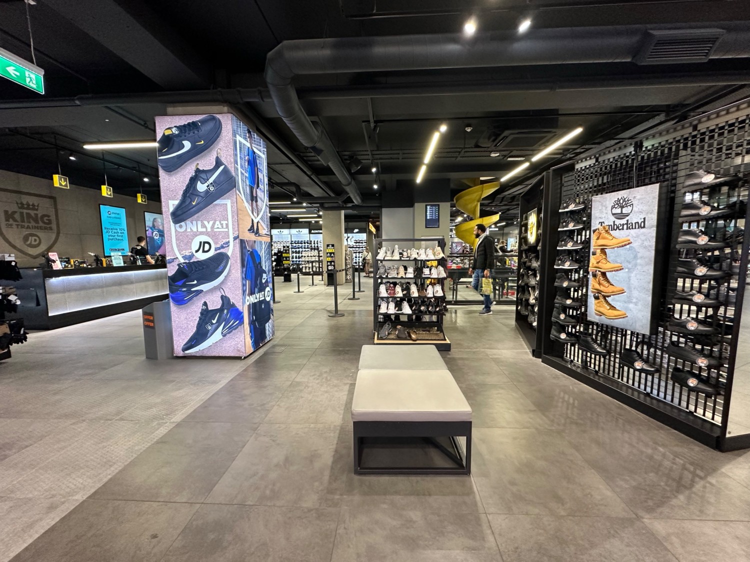 From after second central shoe rack facing right. Bench ahead with mini shoe rack after it. Path to left leads to far left area. Pillar to far left.