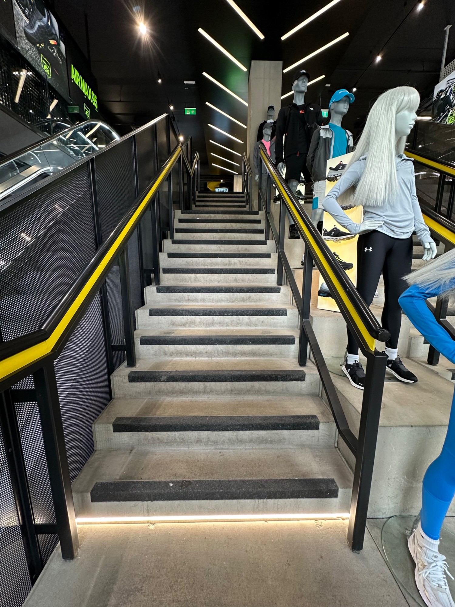 From top of first flight of stairs facing straight. Black and yellow handrail on left and right of second flight of stairs straight ahead.