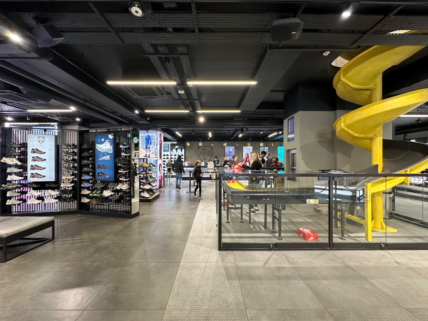 From display area facing straight. Shoe slide display area on right. Bench and back-left shoe display on left. Path ahead leads to till.