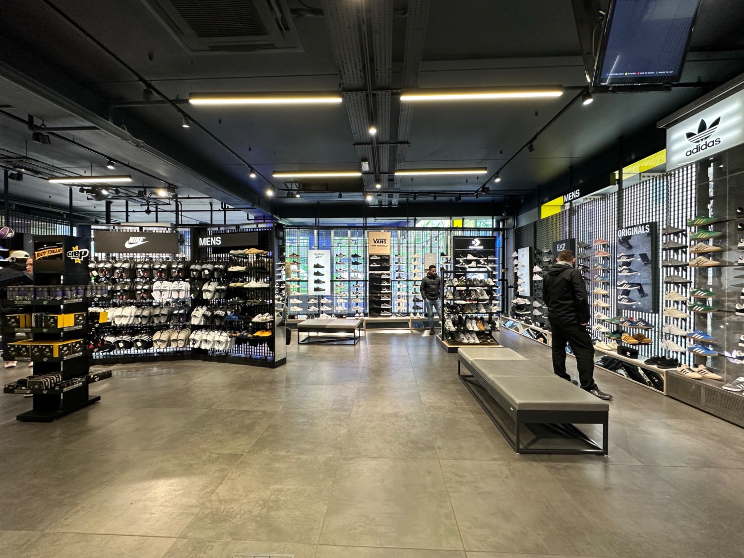 From after first pillar looking left. Bench along right of path. Shoe displays along left, back and right wall ahead. Bench in far left corner.