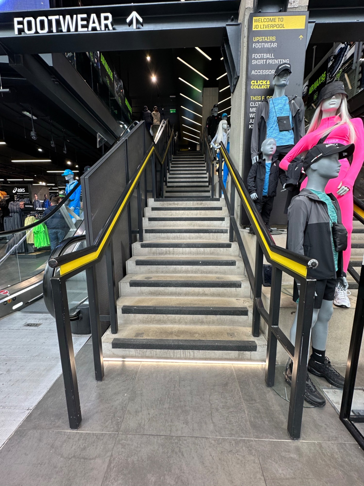 From foot of first flight of stairs facing straight. Black and yellow handrail on left and right of stairs straight ahead.