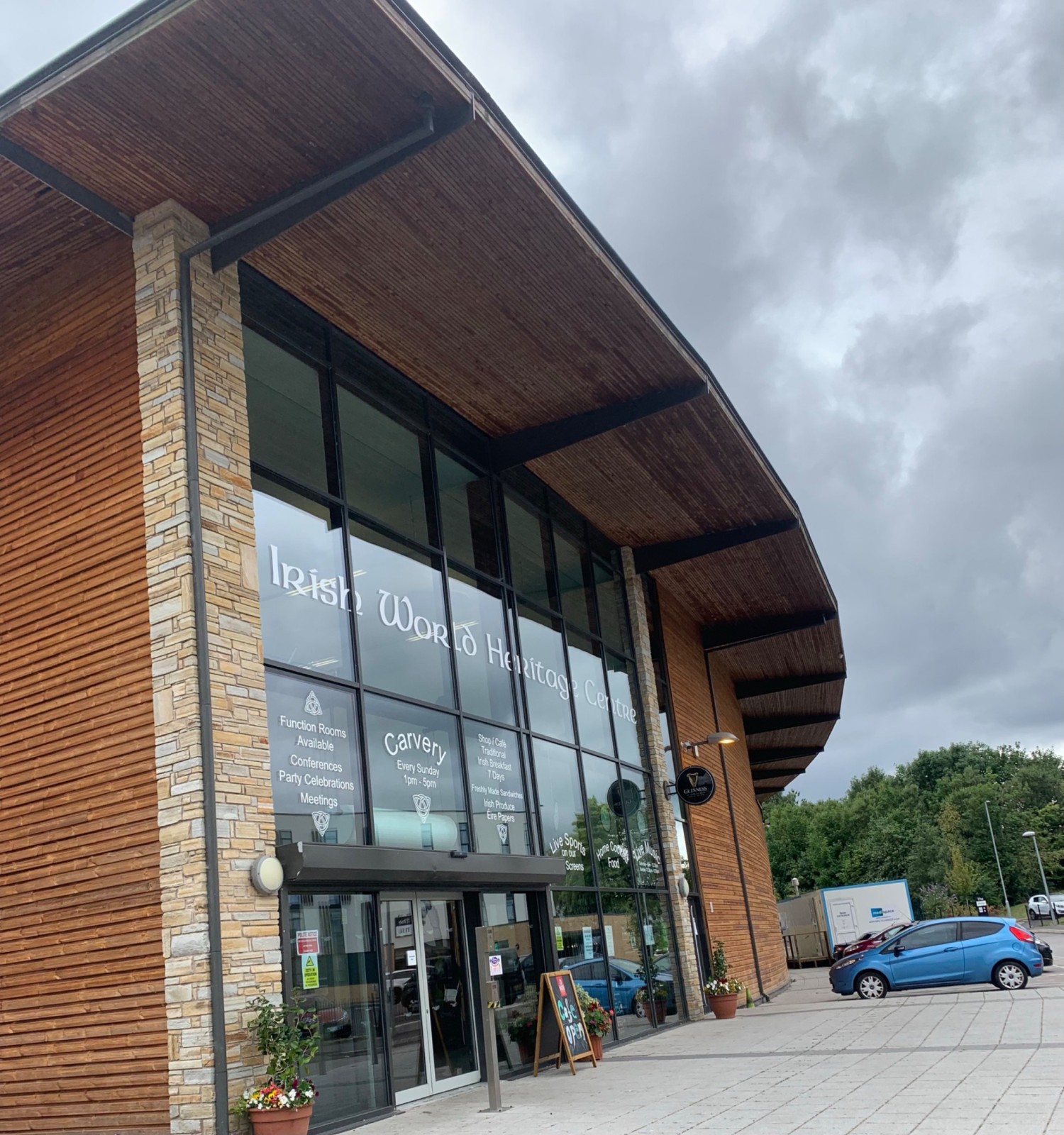 Step free ramp from road to vide pavement, then automatic glass sliding doors to enter the building. Blue badge parking to the right of the image.
