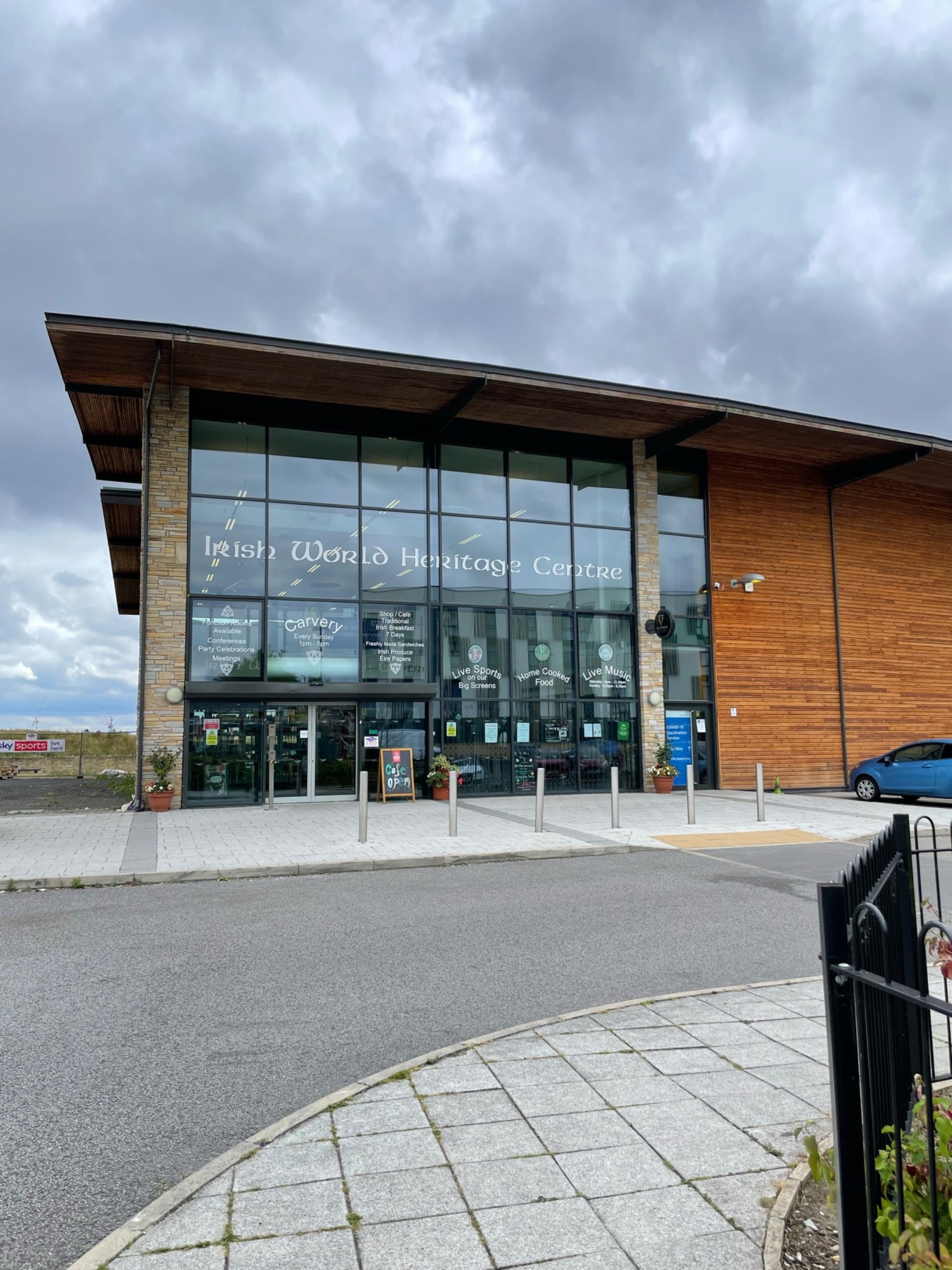 Step free ramp from road to vide pavement, then automatic glass sliding doors to enter the building. Blue badge parking to the right of the image.