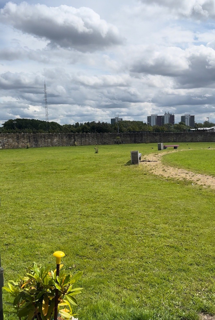View of the grass, dirt path and benches, plus the surrounding stone wall
