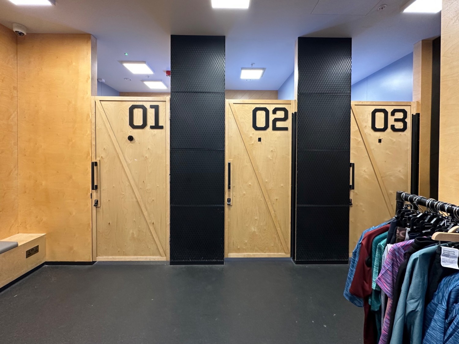 From right of waiting table at end of entrance facing straight, fitting rooms along back wall. Clothing rack to right.
