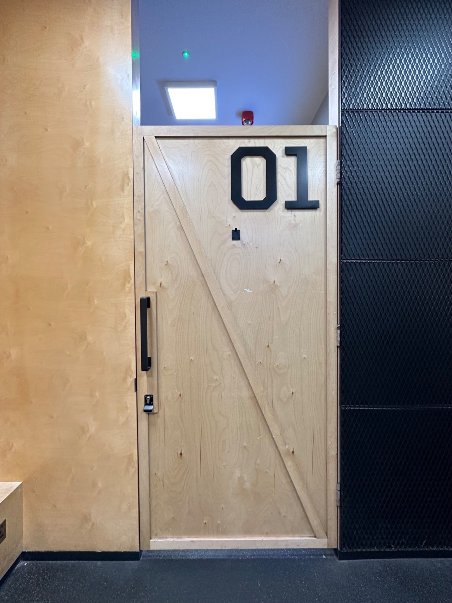 From waiting area facing straight, wooden door ahead. Black handle on left. Key required. Pull to open.