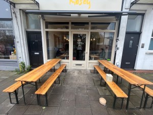 From sidewalk facing venue. Outdoor seating to left and right. Path down centre leads to ramp and main entrance.