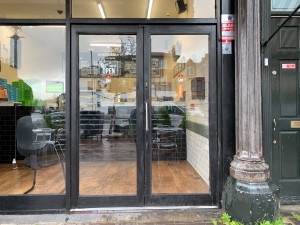 Glass double doors with black frames. Push on silver metal handle on left of right door to open.