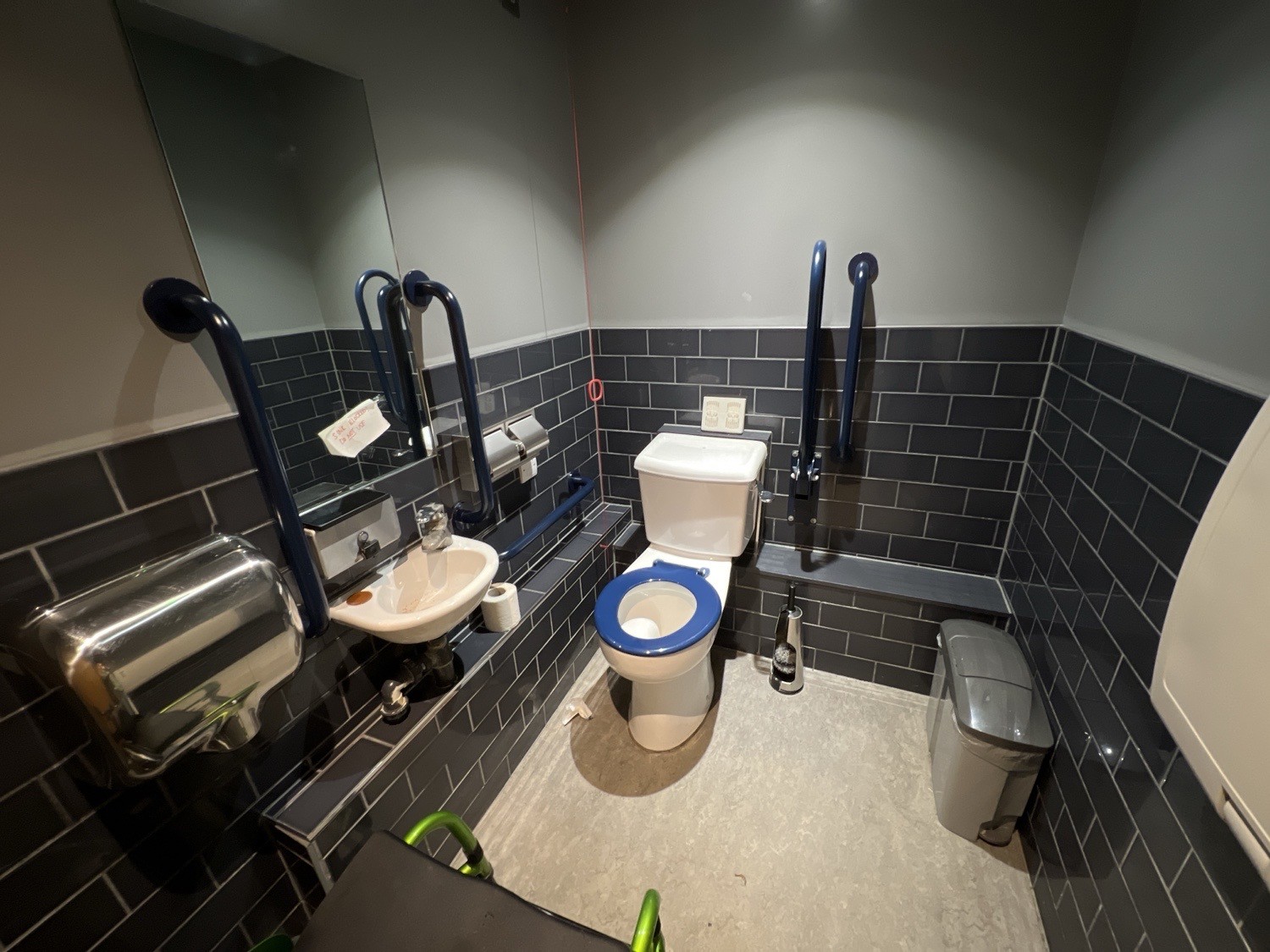 The inside of a disabled bathroom. On the right is a baby changing table. The toilet is directly in front of the door where the camera is angled from
