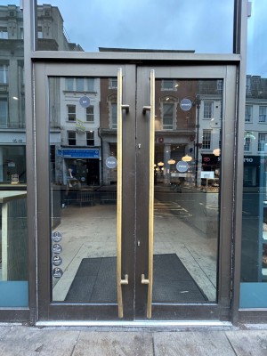 Double glass doors with dark brown frame. Push gold vertical handles in middle to open.